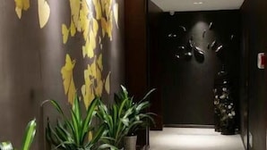 A hallway with a wall decorated with yellow leaves and a dark wall with a light fixture. There are potted plants at the end of the hallway. - GreenTree Inn Taizhou Taixing Middle Guoqing Road Business Hotel (Taizhou)