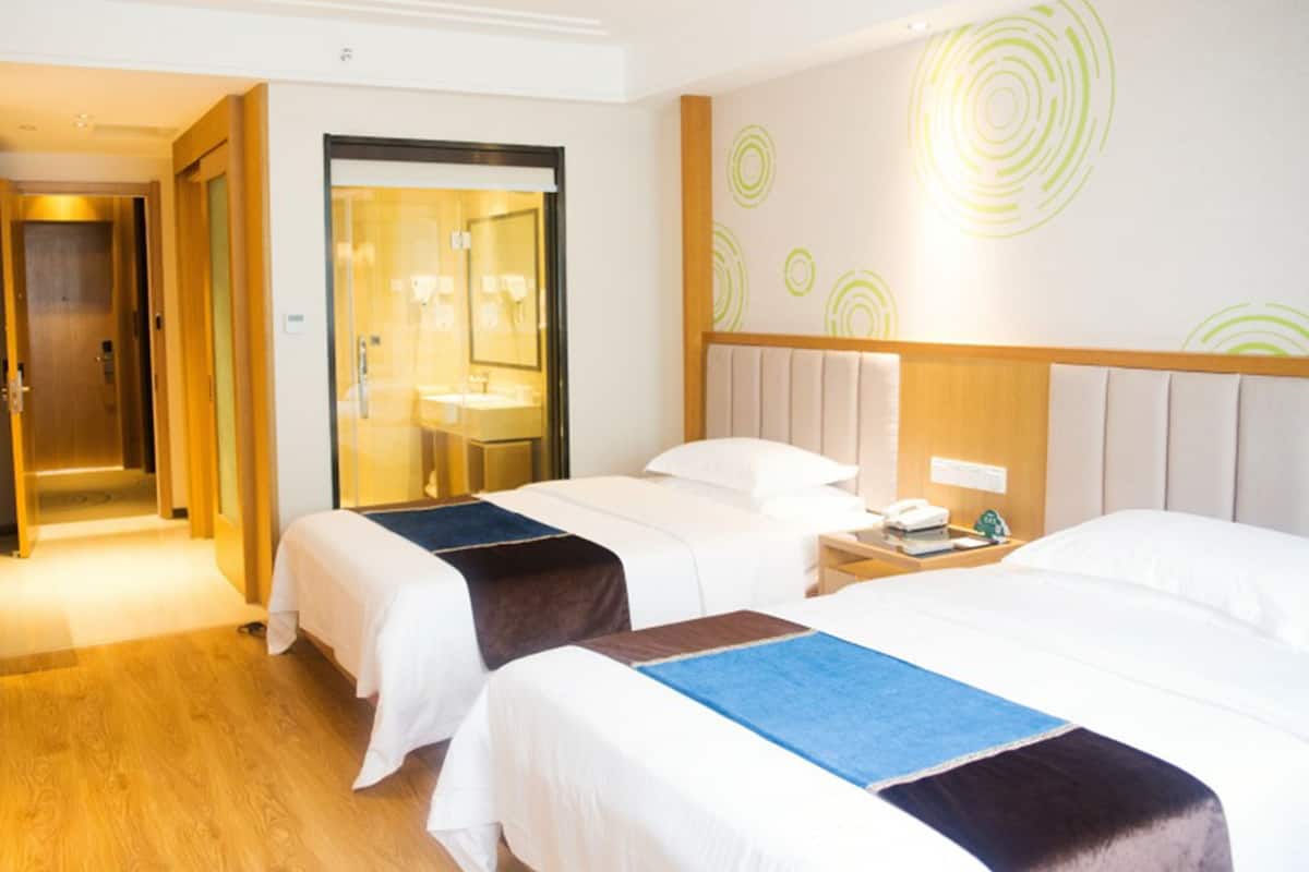A hotel room with two beds, a bathroom, and a hallway.