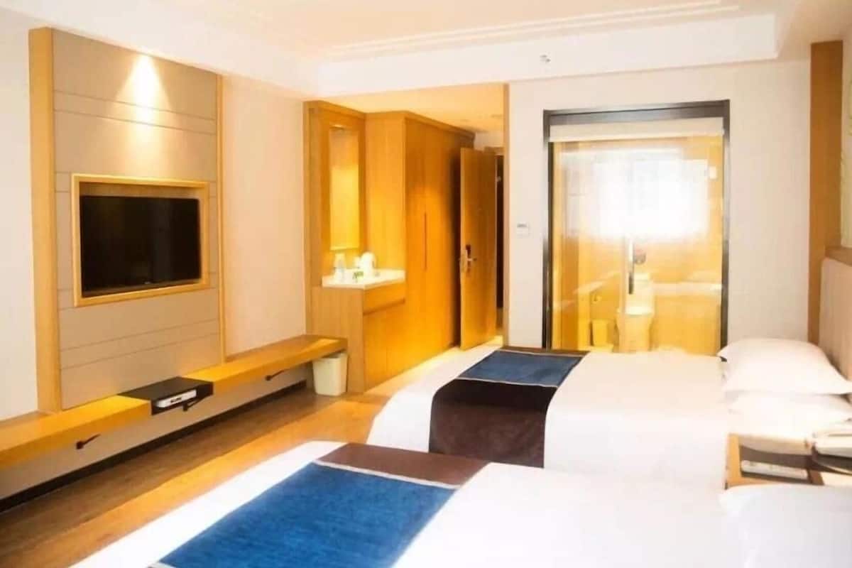 A hotel room with two beds, a TV, a mirror, a bedside table, and a wardrobe.