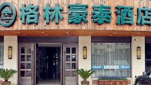 A hotel entrance with a wooden facade, glass doors, and potted plants. - GreenTree Inn Taizhou Taixing Middle Guoqing Road Business Hotel (Taizhou)