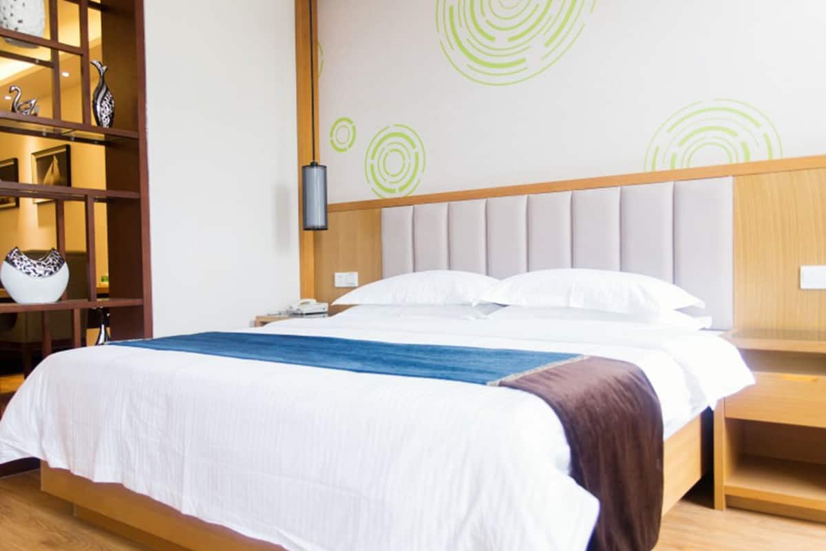 A hotel room with a bed, wooden headboard, a nightstand, a lamp, and decorative wall art.