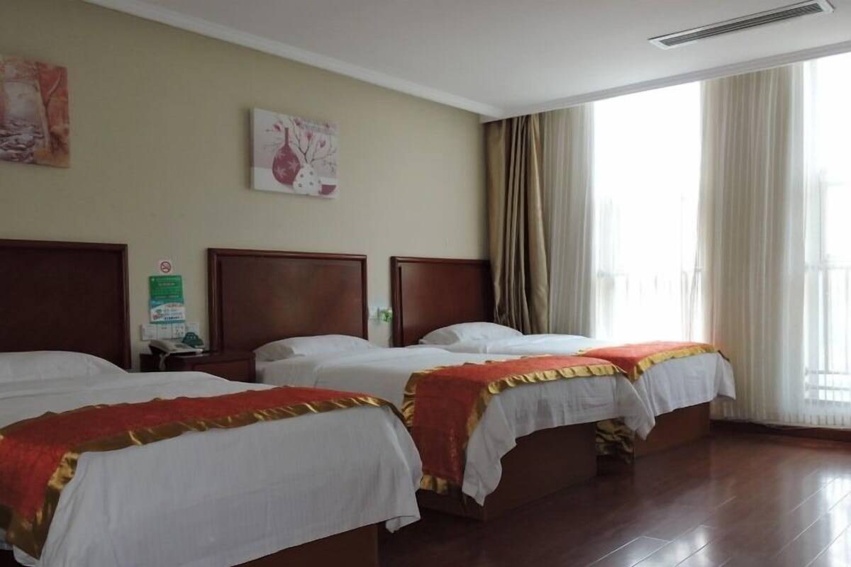 A hotel room with two beds, wooden headboards, a large window with curtains, and a wall-mounted sign.
