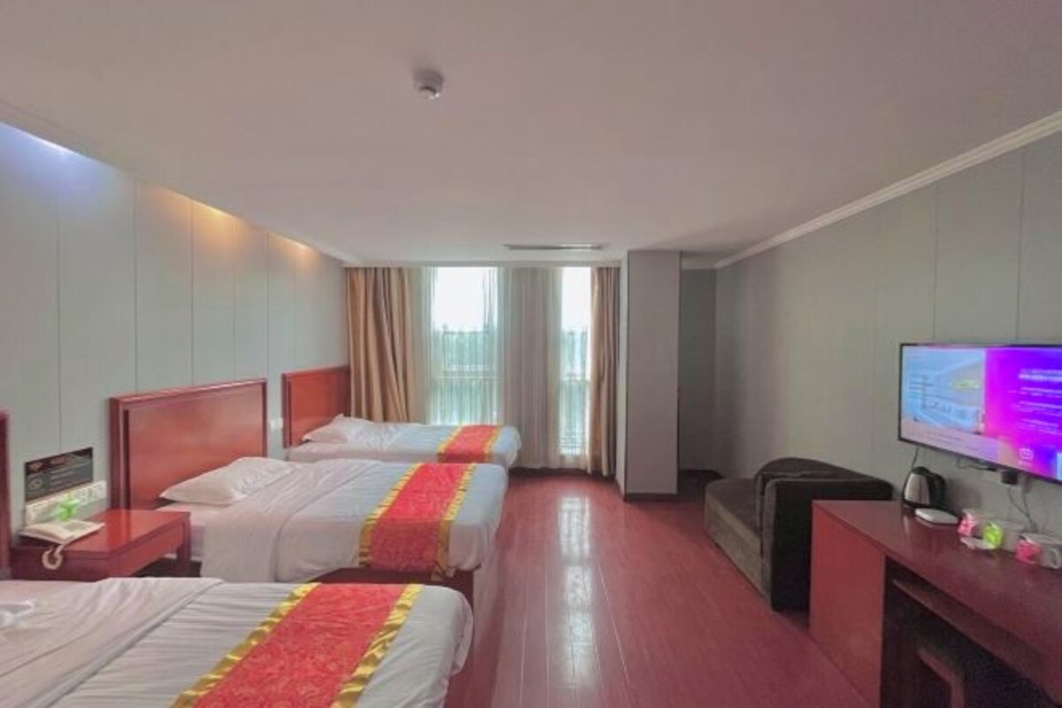 A hotel room with two beds, a TV, a desk, and a window with curtains.