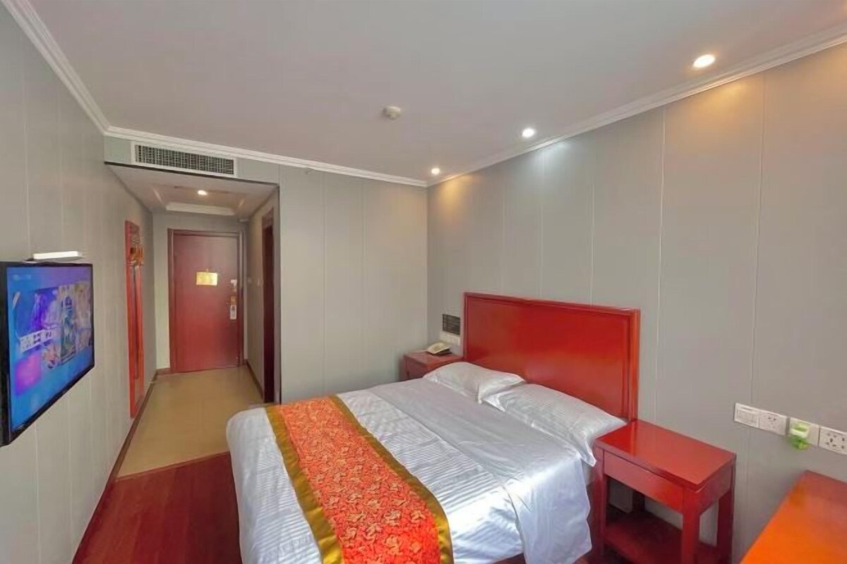 A hotel room with a bed, a nightstand, a TV, and a door leading to another room.