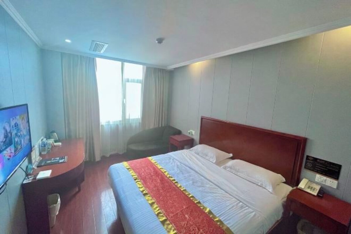 A hotel room with a bed, a desk, a chair, and a television.