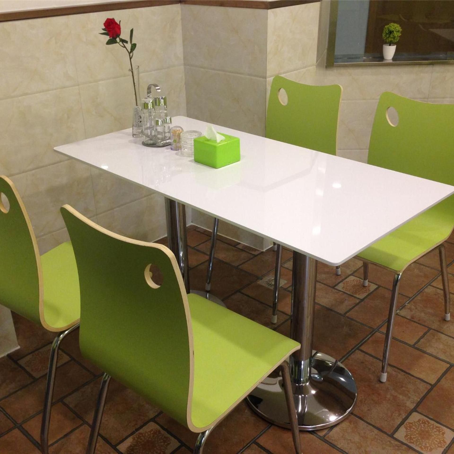 A white table with four green chairs, a vase with a single red rose, and a green tissue box on the table.