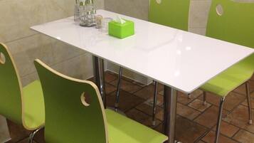 A white table with four green chairs, a vase with a single red rose, and a green tissue box on the table.