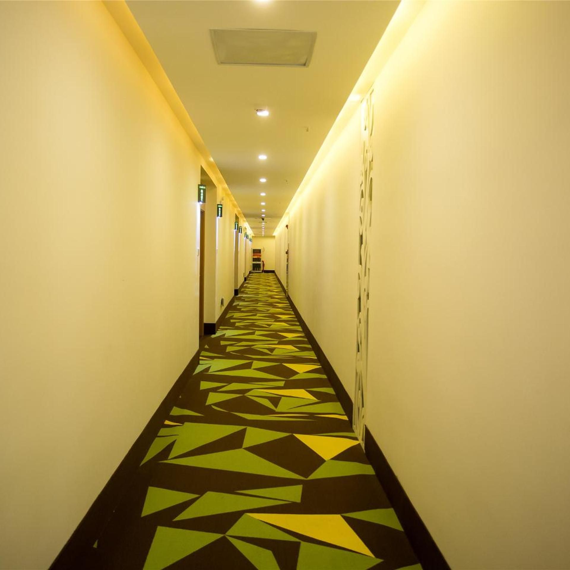 A long, narrow hotel corridor with a patterned floor and doors on both sides.
