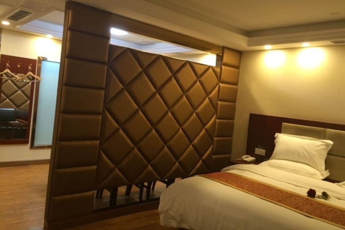 A hotel room with a large bed, a padded headboard, a bedside table with a phone, and a mirror.