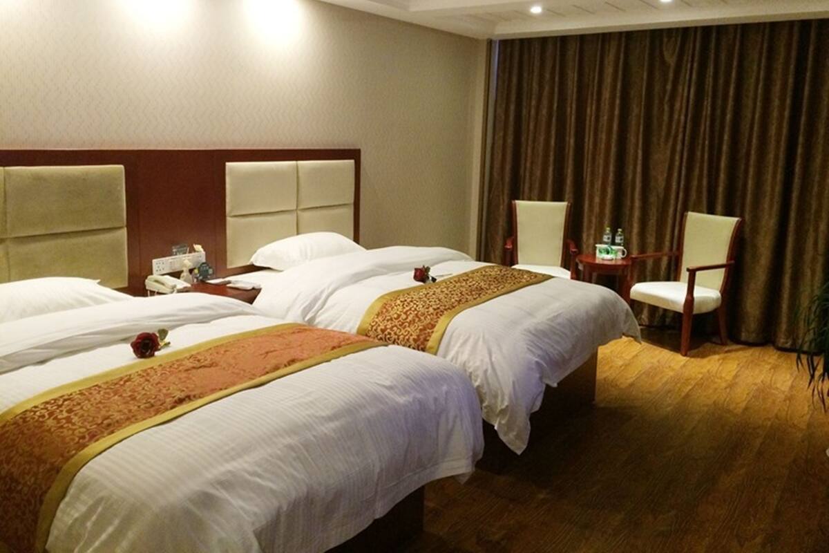 A hotel room with two beds, a wooden headboard, a small table with a phone and a cup, and a chair.