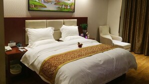 A hotel room with a large bed, a headboard, a nightstand with a phone, a chair, and a painting on the wall. - GreenTree Inn Suqian Sihong Passenger Station Zhongyuan Logistics District Hotel (Suqian)