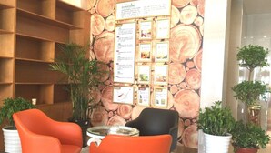 Uma área de recepção com estantes de madeira, um mural de avisos e duas cadeiras laranja.