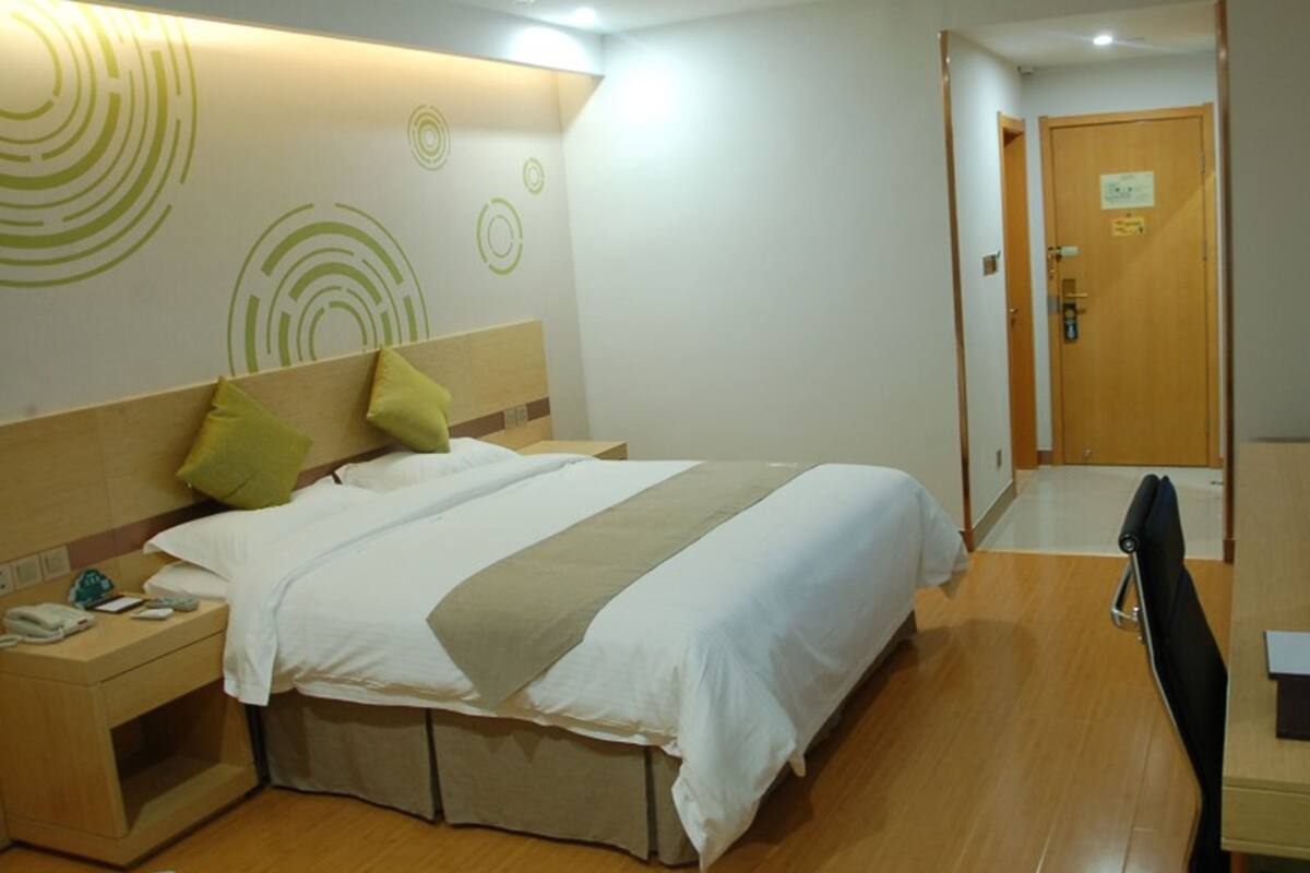 A hotel room with a bed, bedside table, and a desk with a chair.