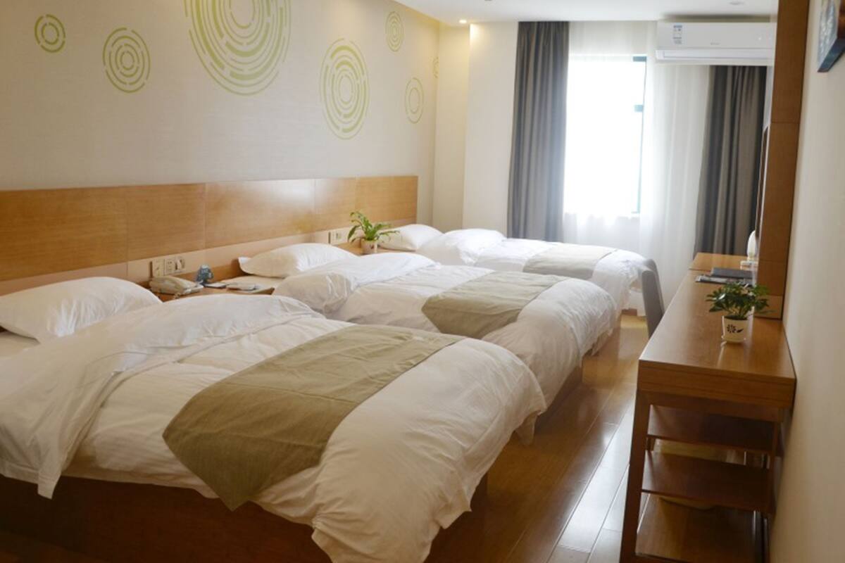 A hotel room with three beds, a wooden headboard, a desk, and a window with curtains.