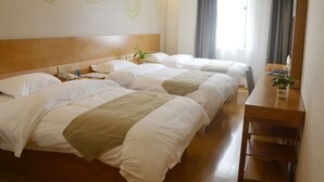 Quarto de hotel com três camas, cabeceira de madeira, escrivaninha e janela com cortinas.
