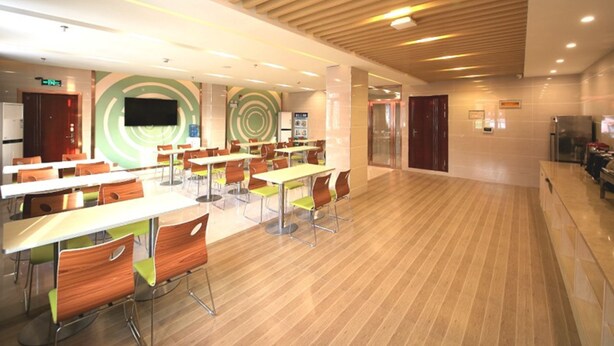 Uma sala de jantar espaçosa com várias mesas e cadeiras, design moderno no teto e uma tela grande na parede.