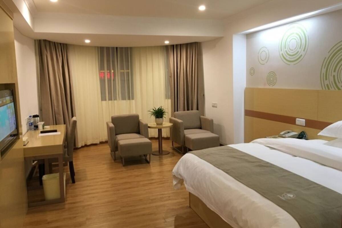 Una habitación de hotel con una cama, dos sillones, una mesita con una planta, un escritorio con una computadora y un televisor.
