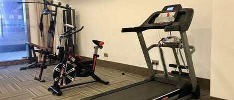 A fitness room with a treadmill, stationary bike, and weight machine.