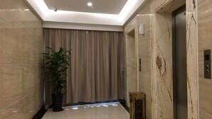 A modern hallway with a marble floor, a potted plant, a closed elevator, and a curtain. - GreenTree Inn Zhongshan Fusha Town Hotel (Zhongshan)