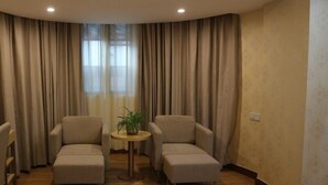 A room with two armchairs, a small round table with a plant, and a window with curtains. - GreenTree Inn Zhongshan Fusha Town Hotel (Zhongshan)