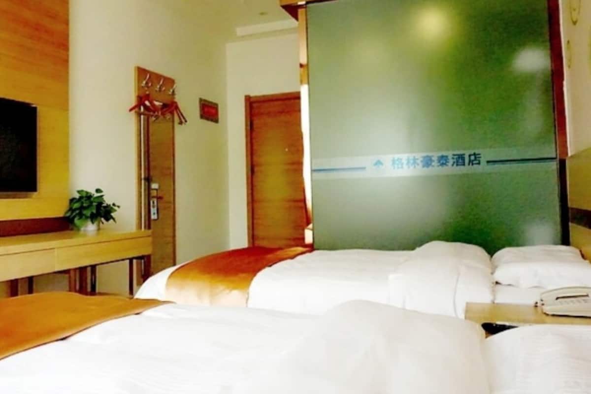 A hotel room with a bed, a bedside table, a plant, and a wall with a sign.