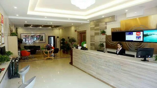 A hotel reception area with a marble counter, a television screen, and a receptionist. - GreenTree Inn Langfang GuAn County Xinyuan Street Express Hotel (Langfang)