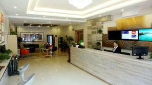 A hotel reception area with a marble counter, a television screen, and a receptionist. - GreenTree Inn Langfang GuAn County Xinyuan Street Express Hotel (Langfang)