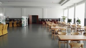 Un grand espace dédié à la salle à manger, avec plusieurs tables et chaises, un coin cuisine et de grandes fenêtres laissant entrer la lumière naturelle.