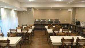 Un restaurant avec des chaises et des tables en bois, un espace cuisine équipé d’appareils électroménagers et un sol carrelé.