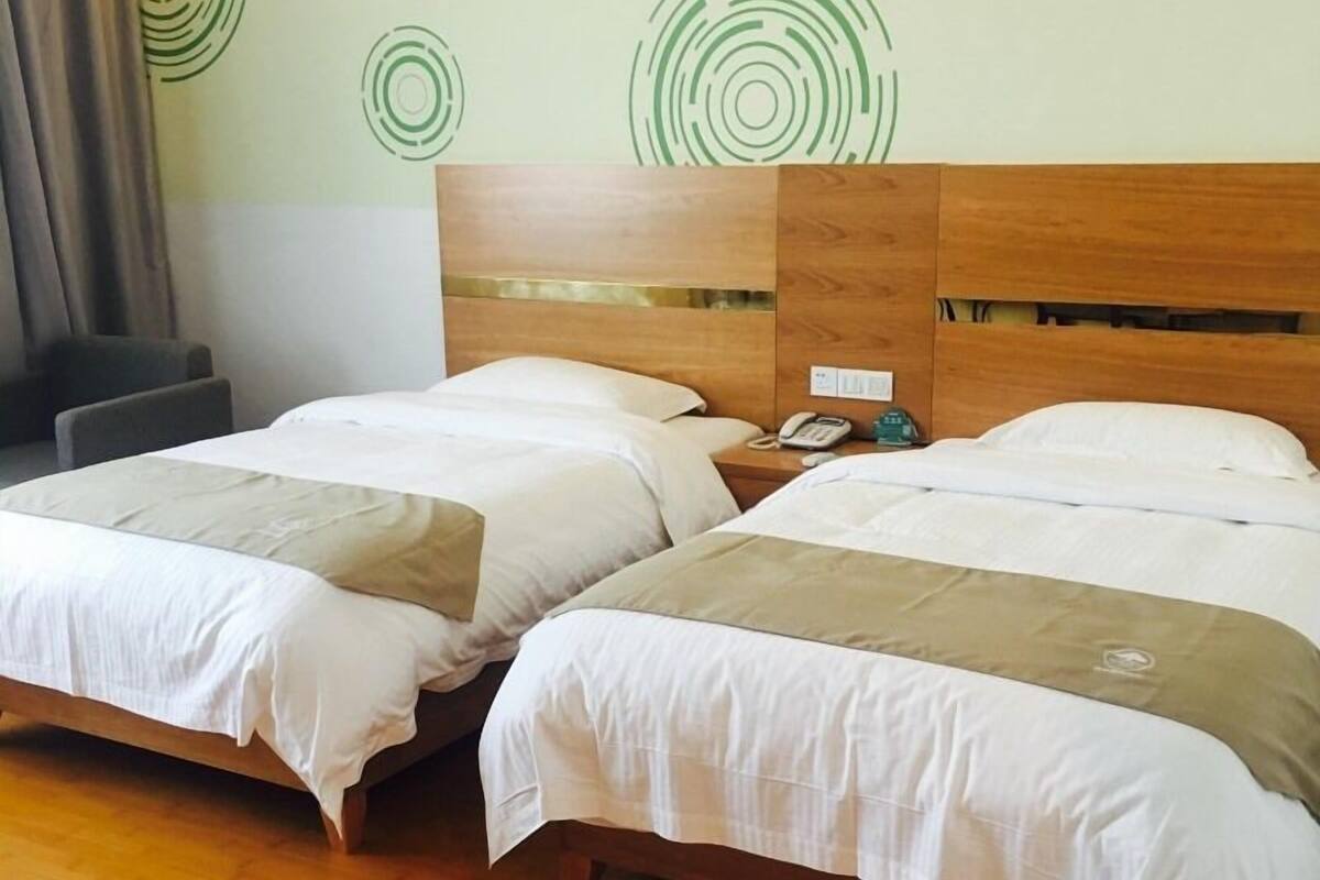 Ein Hotelzimmer mit zwei Betten, einem Holzkopfende, einem Nachttisch mit Telefon und einer Wand mit kreisförmigem Muster.