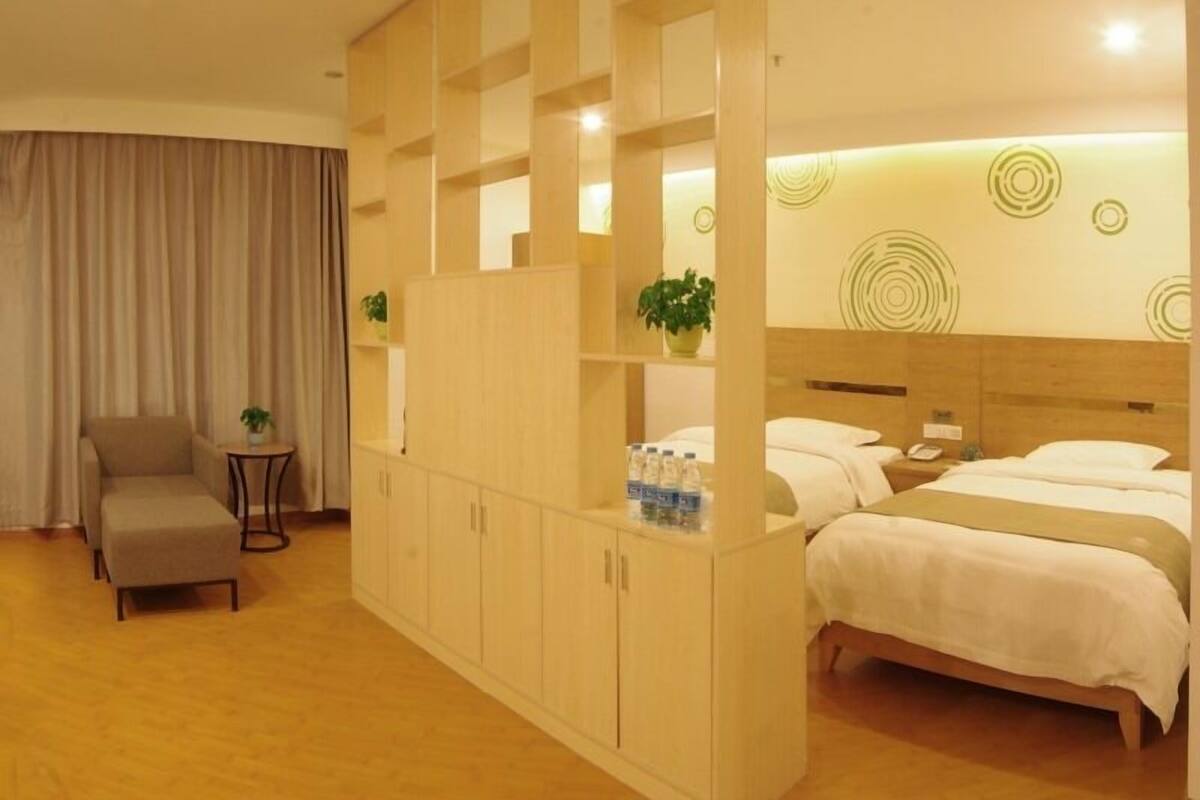 Ein Hotelzimmer mit einem Bett, einem Sofa, einem kleinen Tisch mit Pflanze und einem Schrank mit Wasserflaschen.