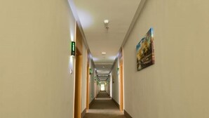 Un largo pasillo de hotel, estrecho, con puertas a ambos lados, carteles de salida verdes y un cartel en la pared derecha.