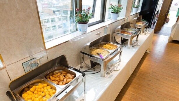 Montaje de bufé con diversos alimentos en recipientes metálicos, dispuestos sobre una barra con un rebozo de azulejos y una ventana con vista a la ciudad.