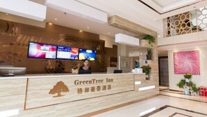 Un mostrador de recepción de hotel con una pantalla digital mostrando información, una recepcionista y un letrero que indica el nombre del hotel 'GreenTree Inn'.