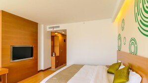 A modern hotel room with a wooden floor, a bed with white bedding and two pillows, a TV mounted on the wall, and a small table. - GreenTree Inn Wuhu Fangte Four Phase Wanchun Fortune Plaza Hotel (Wuhu)