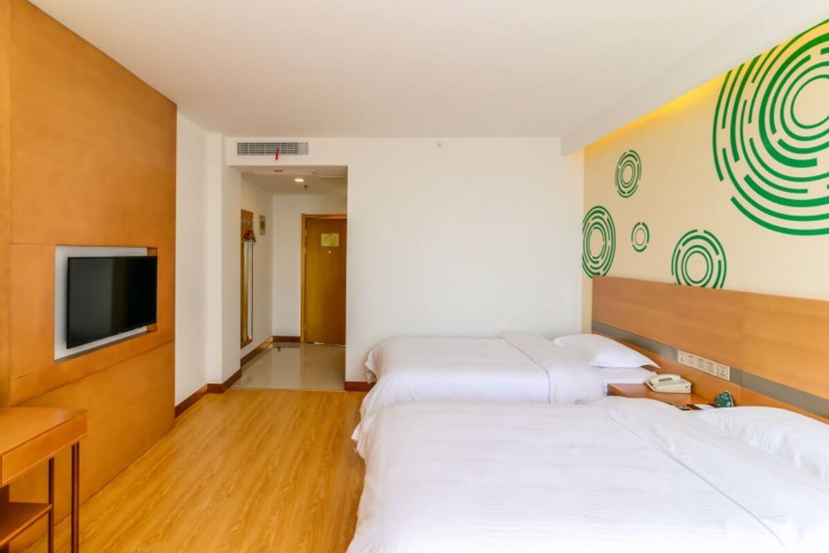 A hotel room with two beds, a flat-screen TV mounted on the wall, a wooden floor, and a wall with green circular patterns.