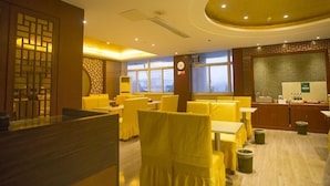 A restaurant with yellow chairs and tables, a clock on the wall, and a view of the city through large windows. - GreenTree Alliance Chuzhou Laian County Development District Jingyi Road Hotel. (Chuzhou)