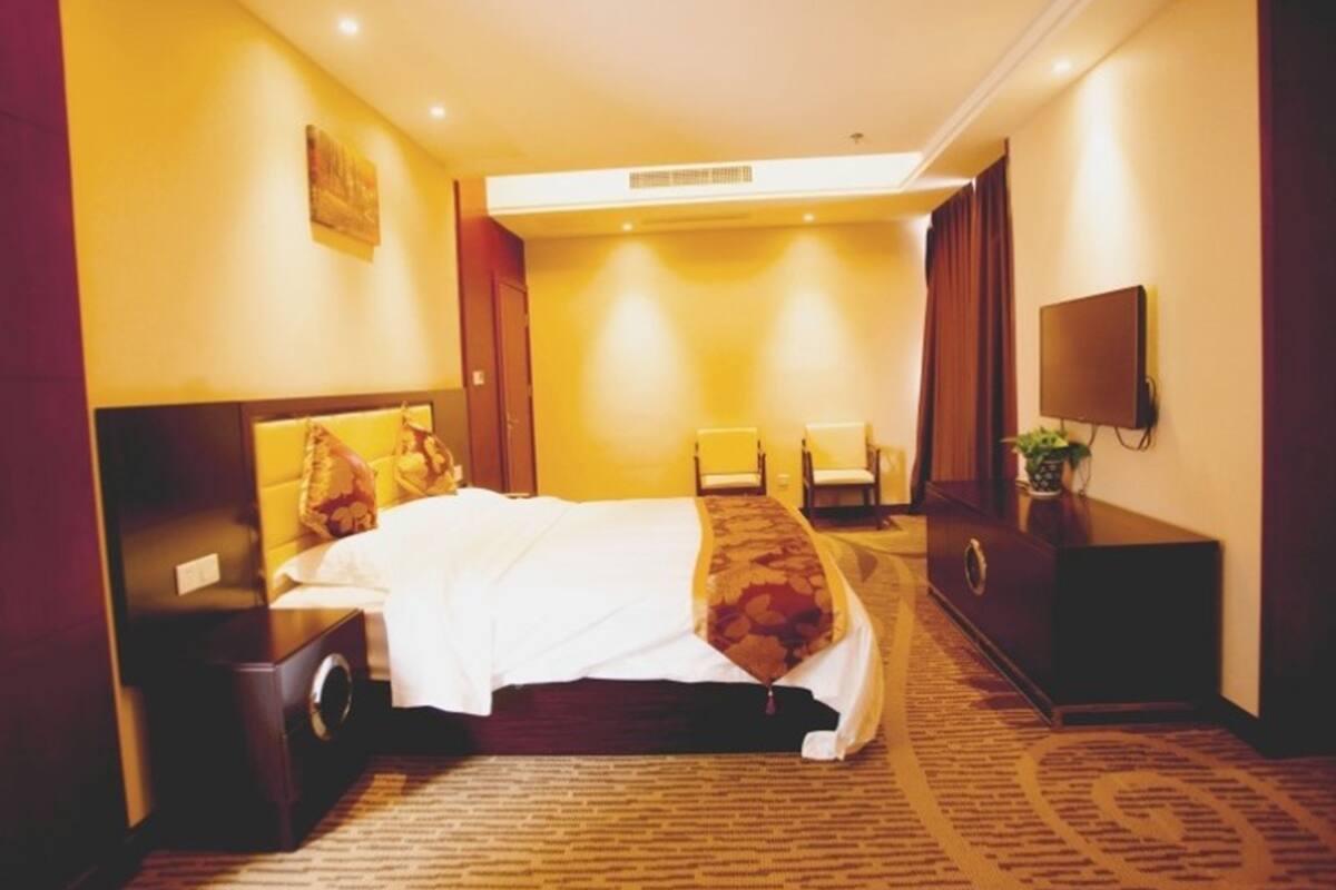 Una habitación de hotel con una cama grande, un escritorio con silla, una televisión y piso alfombrado.