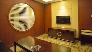 A modern hotel room with a large round window, a flat-screen TV mounted on the wall, a dark wooden coffee table, and a patterned carpet. - GreenTree Alliance Chuzhou Laian County Development District Jingyi Road Hotel. (Chuzhou)