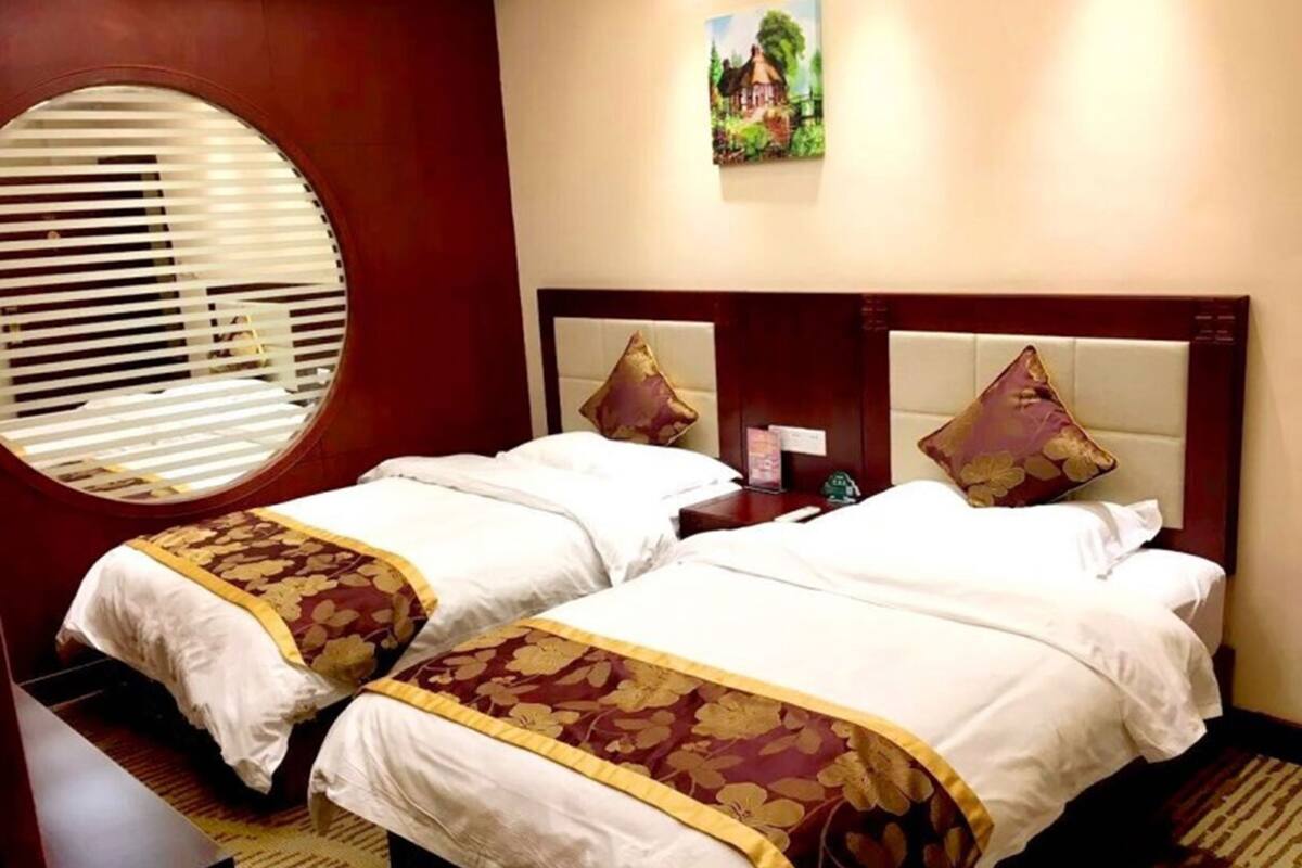 Habitación de hotel con dos camas, un espejo redondo, un cuadro en la pared y una mesita de noche con una lámpara.