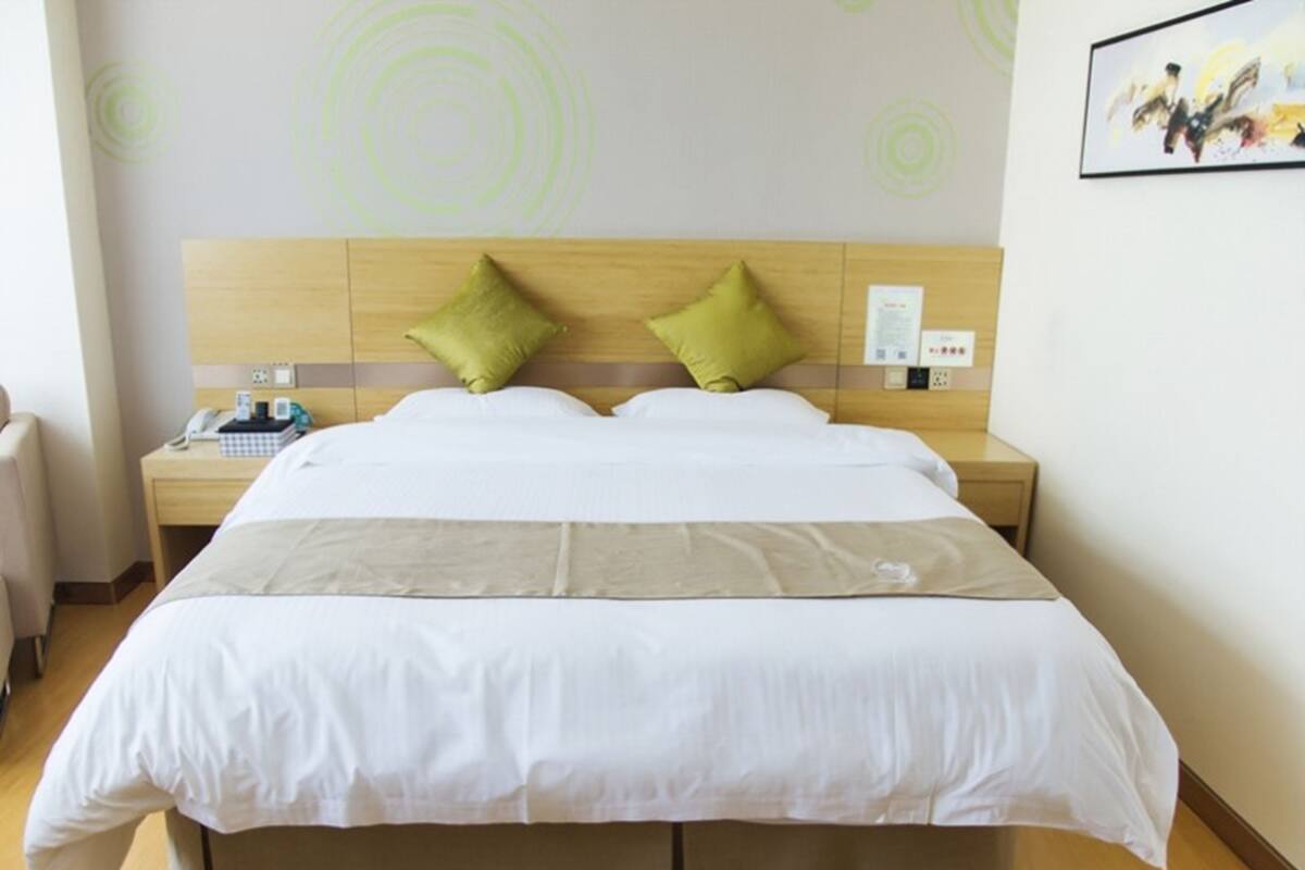 A hotel room with a large bed, two pillows, a bedside table with a phone, and a wall with a circular pattern.