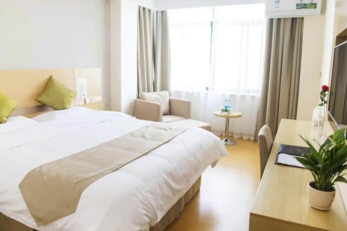 Ein Hotelzimmer mit einem großen Bett, einem Schreibtisch, einem Sessel, einem kleinen Tisch und einer Topfpflanze.
