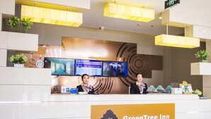 Un comptoir d’accueil se trouve dans le hall du GreenTree Inn, avec deux réceptionnistes, un panneau d’affichage numérique et un panneau indiquant la direction de la sortie.