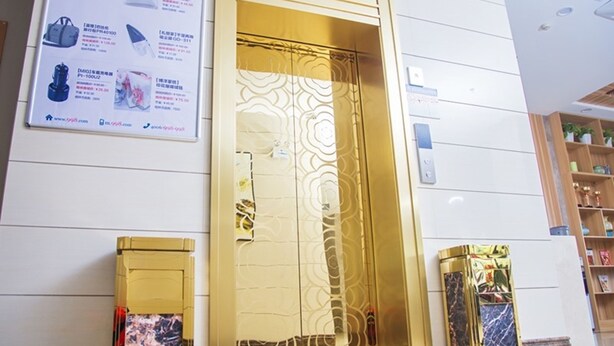 Une entrée d’hôtel moderne avec une porte d’ascenseur dorée, un comptoir de réception et un panneau d’affichage présentant des informations sur les produits.