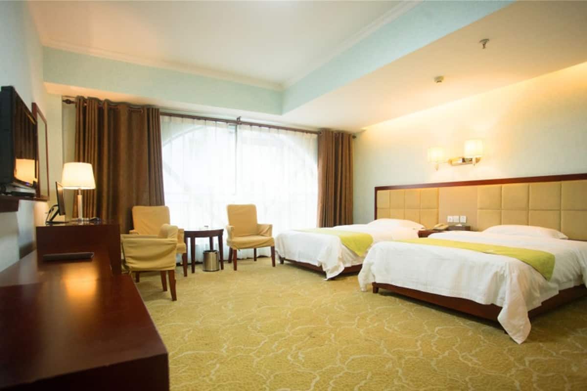 Habitació d'hotel amb dos llits, escriptori, cadira, làmpada i finestra amb cortines.