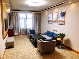 Quarto de hotel moderno com sofá, mesa pequena, televisão e janela com cortinas.