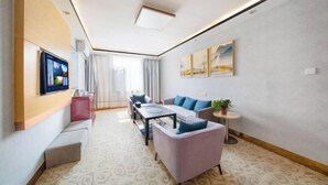 A modern hotel room with a sofa, a small table, a TV mounted on the wall, and a window with curtains. - GreenTree Inn Express Hotel (Binzhou Wudi Ancient City) (Binzhou)