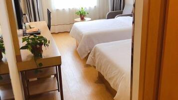 A hotel room with two beds, a desk with a chair, a small table with a plant, and a window with curtains.