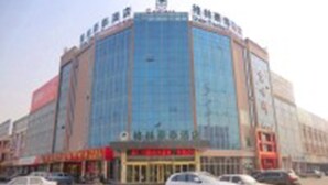 A multi-story building with a glass facade, several ground-level shops, and parked cars in front. - GreenTree Inn LinYi Lanshan District LinXi No.11 Road Express Hotel (Linyi)