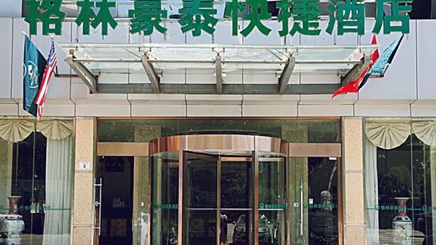 A hotel entrance with a glass revolving door, a covered entrance area, and flags on either side. - GreenTree Inn Lianyungang Ganyu South Station Express Hotel (Lianyungang)